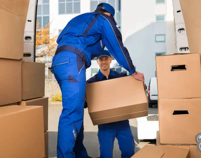Professional movers in blue uniforms loading cardboard boxes into a moving van for a house removal service.