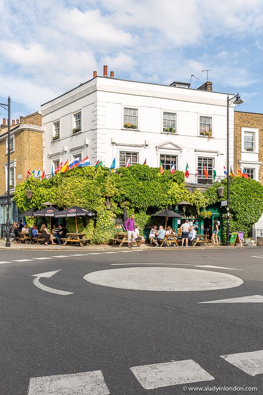 Barnsbury London street corner with ivy-covered pub building, outdoor seating, and pedestrians enjoying cafés near Barnsbury Square on a bright day