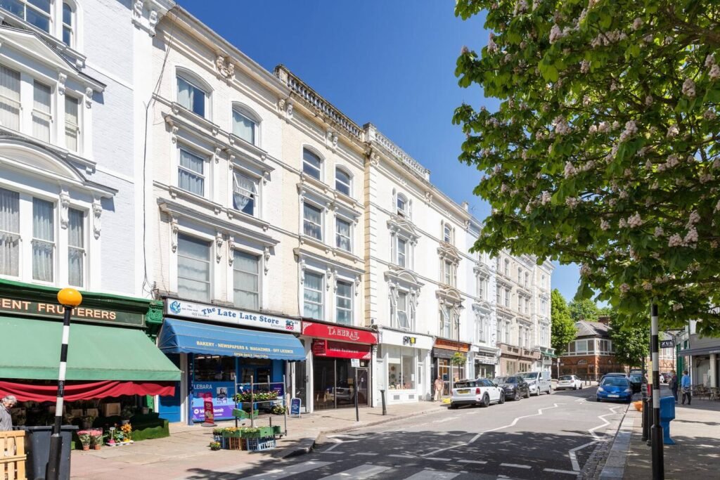 Belsize Park London high street with period buildings, local shops, parked cars and leafy trees along a quiet residential road near Haverstock Hill