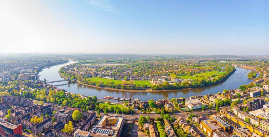 Aerial view of West London showing the River Thames winding around residential neighbourhoods, green parks and riverside homes near Chiswick and Barnes on a clear day